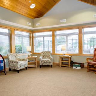 A cozy living room with ample natural light, featuring several chairs and large windows.