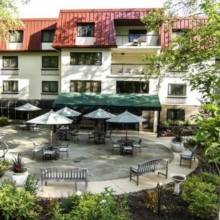 A view of a hotel building with outdoor seating on a patio surrounded by trees.