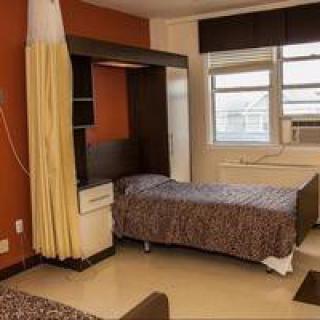 A hospital room with a single bed, large window, curtain, and air conditioning unit.