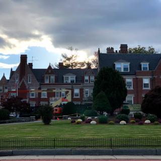 A charming brick building set against a dramatic sky, surrounded by neatly trimmed lawns and trees.