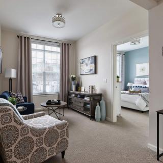 A modern living room with neutral tones and a glimpse into the bedroom.