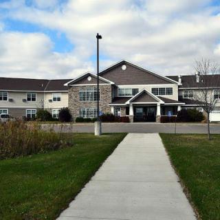 A well-maintained residential building with a paved walkway surrounded by green grass and a cloudy sky.