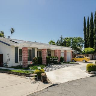 A suburban house with a driveway, front yard, and surrounding trees under a clear blue sky.