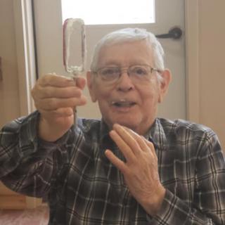 An elderly man joyfully holding up a small object, capturing a moment of delight indoors.