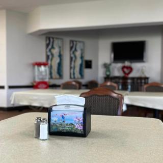 A cozy dining area with tables, chairs, and a napkin holder, featuring a television and artwork.