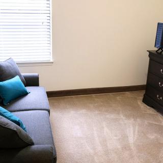 A simple living room with a gray sofa, turquoise pillows, and a television on a stand.