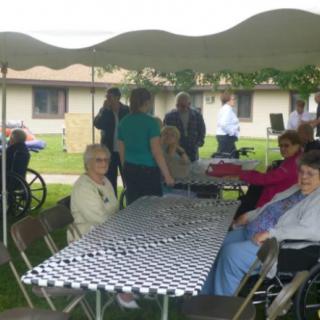A group of people gathered under a tent with chairs and tables set up outdoors.