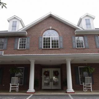 A two-story brick building with a prominent entrance, featuring columns and multiple windows.