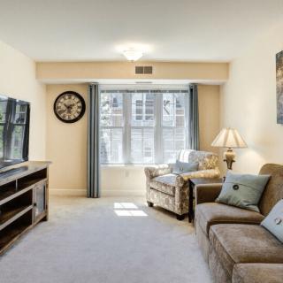 A cozy living room featuring a sofa, armchair, and television with a large window providing natural light.