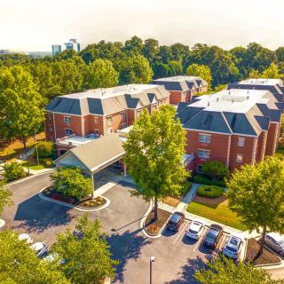 Aerial view of a suburban apartment complex surrounded by trees with a parking lot.