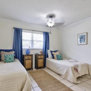 A cozy bedroom with two twin beds, blue curtains, and decorative pillows in a neutral color scheme.