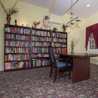 A cozy library with a wall of bookshelves, a wooden desk, and an upholstered chair.
