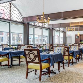 An elegant dining area with neatly arranged tables and chairs, featuring large windows and a chandelier.