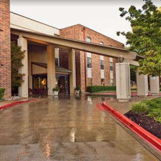 Hotel entrance with driveway and landscaped surroundings.