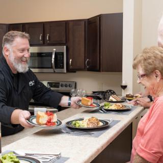 A person serving meals to guests in a kitchen setting.