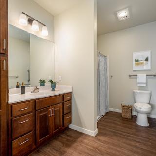 A bright and modern bathroom featuring a wooden vanity, spacious mirror, and clean design elements.