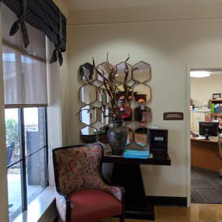 A cozy corner in an office featuring a decorative chair, wall art, and a vase with branches.