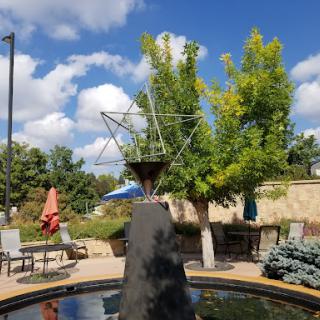 A serene park scene featuring a unique fountain surrounded by lush greenery and under a bright blue sky.
