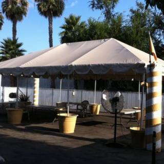 A shaded outdoor seating area with a tent and palm trees in the background.