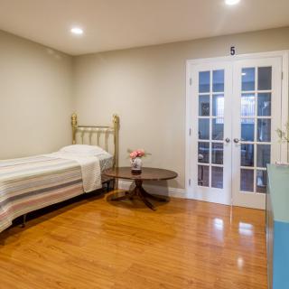 A minimalist bedroom featuring a single bed, wooden flooring, and French doors.
