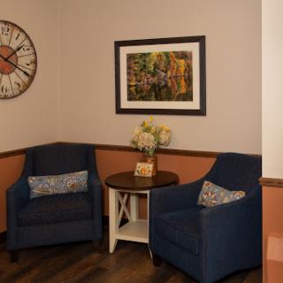 A cozy seating area featuring two blue chairs, a small table, and decorative wall art.