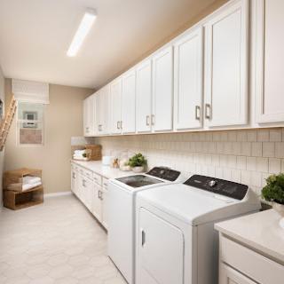 A bright and organized laundry room featuring white cabinetry and modern appliances.