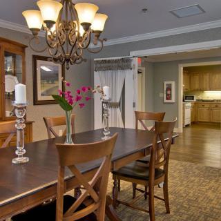 A cozy dining room featuring a wooden table with chairs, adorned with a chandelier, leading into an adjoining kitchen space.