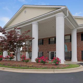 A building with large columns at its entrance, surrounded by landscaping and flowers under a blue sky.