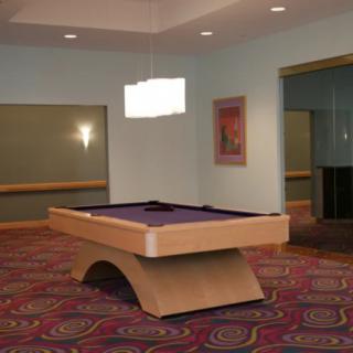 A modern room featuring a uniquely designed pool table with purple felt, complemented by patterned carpeting and contemporary lighting.