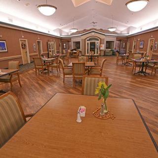 A spacious dining room with wooden floors, neatly arranged tables and chairs, and soft overhead lighting.