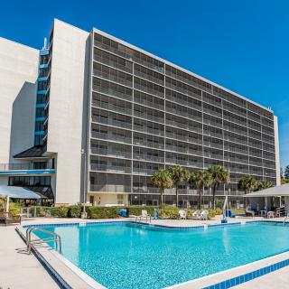 A modern hotel with a large outdoor swimming pool under a clear blue sky.