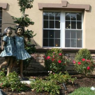 A garden scene featuring a statue of two children next to blooming flowers in front of a house.
