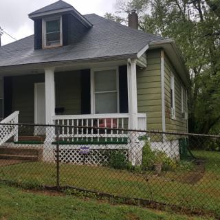 A quaint, single-story house with a front porch and fenced yard.