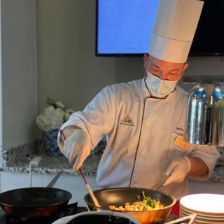 A professional chef wearing a tall white hat prepares food in a kitchen.