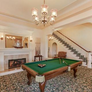 A vintage-style billiard room featuring a pool table, chandelier, and a fireplace.