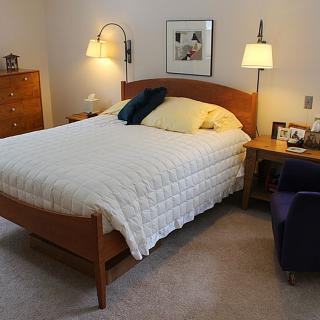 A cozy bedroom with a neatly made bed, nightstands, and warm lighting.