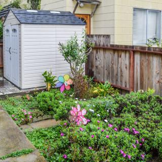A quaint backyard garden with a white storage shed surrounded by vibrant flowers and plants.