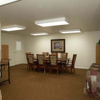 A spacious dining room with a large table and chairs, featuring ceiling lights and a painting on the wall.
