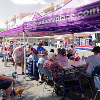 A community gathering with people seated under a purple canopy at an outdoor event.