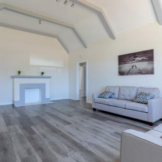A minimalist living room with a modern design, featuring a sofa, fireplace, artwork, and hardwood flooring.