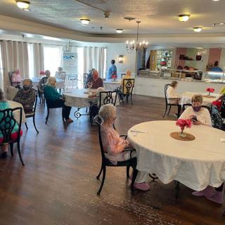 A communal dining area with elderly residents gathered around tables in a senior living facility.