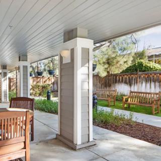 A covered patio with wooden furniture overlooking a garden with benches.