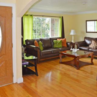 A cozy living room with wooden floors, a leather sofa set, and a large window bringing in natural light.