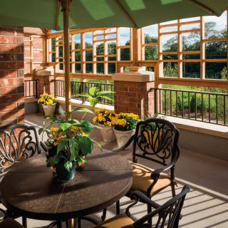 A sunlit patio with elegant furniture and vibrant flowers under a green umbrella.