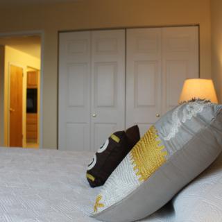 A cozy bedroom with decorative pillows and a warm-lit lamp beside a closet.