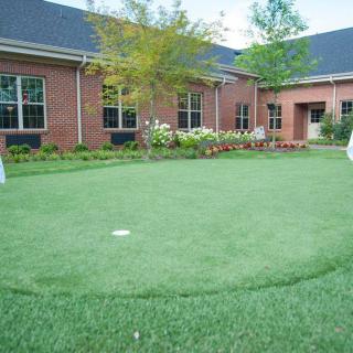 A well-maintained putting green situated in a courtyard surrounded by brick buildings.