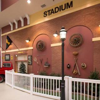 Indoor display with a stadium theme featuring vintage decor on a brick wall, complete with a lamp post and white fence.