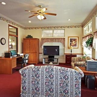 A cozy living room with a television, sofa, desk, computer, and ceiling fan.