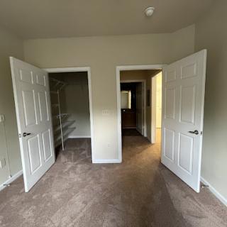 A view of an empty room featuring two open doors, soft carpet, and neutral-colored walls.