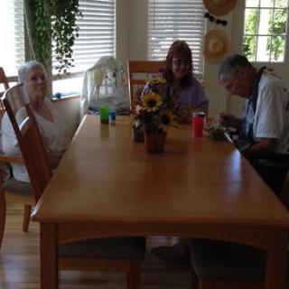 A family gathering around a dining table in a bright room with plants and sunflowers.